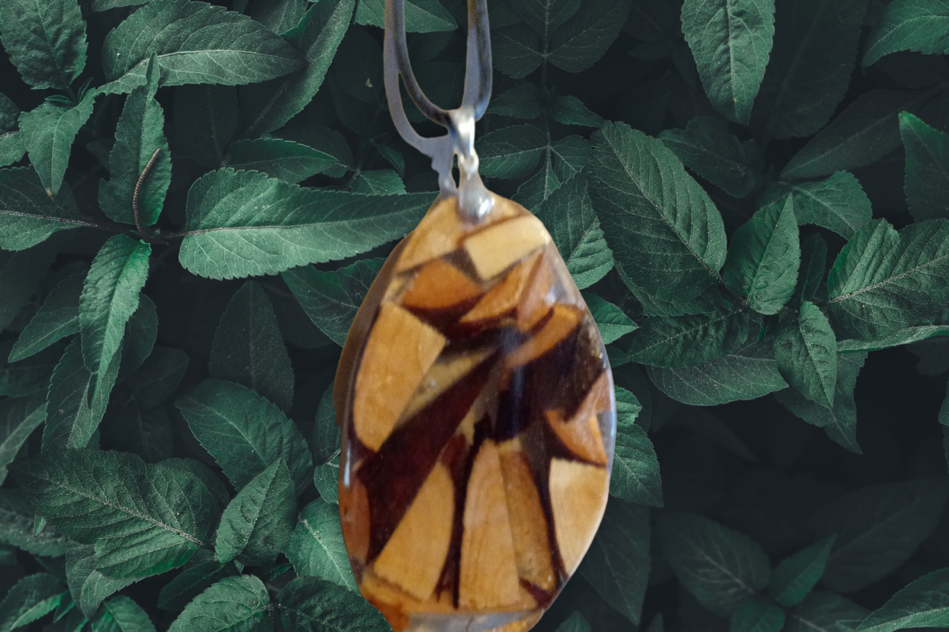 Anhänger aus Holz mit geometrischem Muster auf grünem Blatt-Hintergrund.